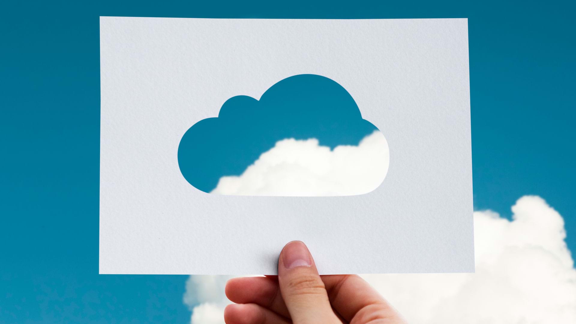 A hand holding a Cloud Paper Cutout against a light blue background, with a real cloud floating by in the corner